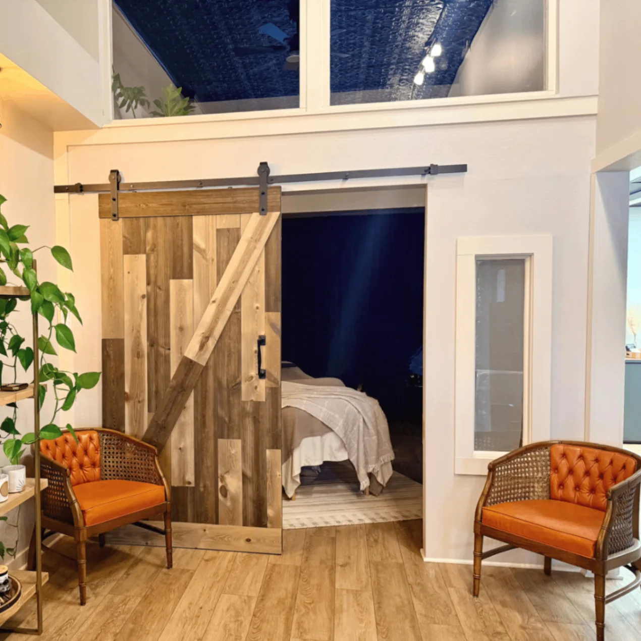 Root + Ritual treatment space in Windsor, Colorado, with a wood barn door, treatment bed, plants, and orange chairs.